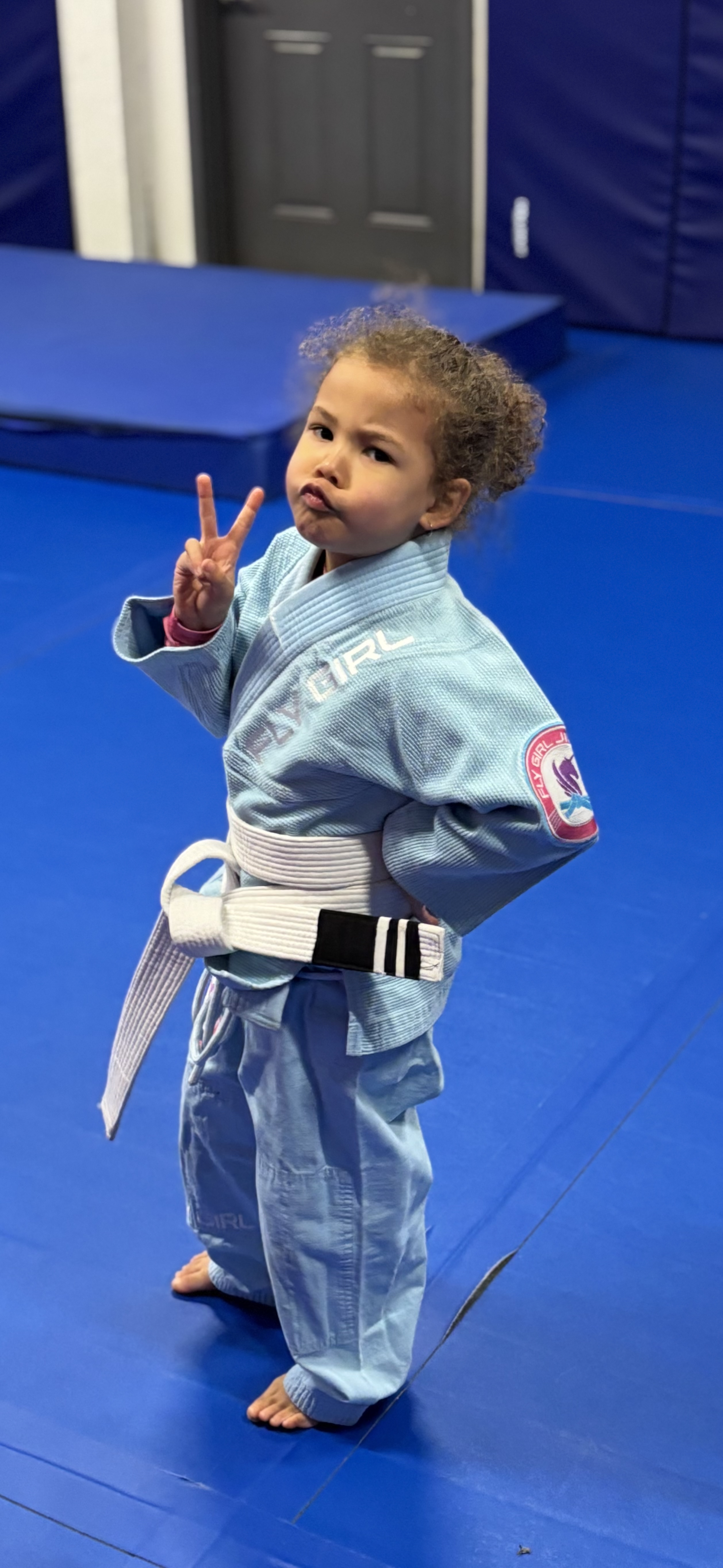 Young girl in light blue training gi making peace sign